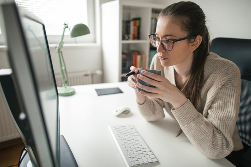 Mulher tomando café, em frente ao computador, em home office