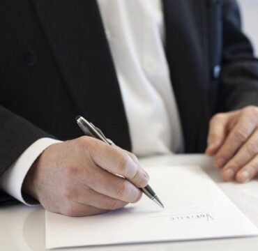 Mãos de homem segurando caneta para assinar um documento em papel